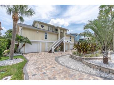 Inviting yellow home with two-car garage, white staircase, and lush tropical landscaping at 633 Soundview Dr, Palm Harbor, FL 34683