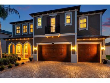 Elegant two-story home featuring a three-car garage and a beautifully lit brick driveway at dusk at 4419 Ortona Ln, Wesley Chapel, FL 33543