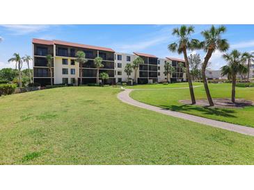 Condominium exterior showing a manicured lawn, mature palms, and a building with multiple screened balconies at 1935 Gulf Of Mexico Dr # G7-304, Longboat Key, FL 34228