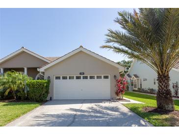 Beige single-story home with a white garage door, a tile roof, and lush tropical landscaping at 1729 Arabian Ln, Palm Harbor, FL 34685