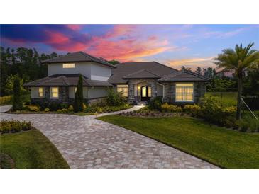 Stunning exterior showcasing stone accents, tile roof, paver driveway, and professional landscaping under a vibrant sunset sky at 17305 Ballmont Park Dr, Odessa, FL 33556