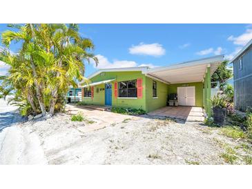 Charming home with a vibrant green exterior, red shutters, blue door, and a covered carport, surrounded by lush trees at 121 86Th Ter, Treasure Island, FL 33706