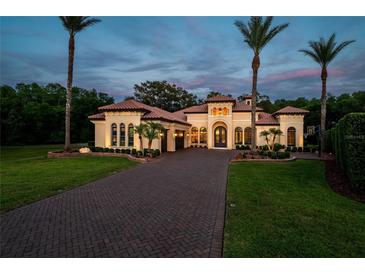 Stunning home features lush landscaping, a paver driveway, and palm trees against a twilight sky at 2680 Keystone Springs Rd, Tarpon Springs, FL 34688