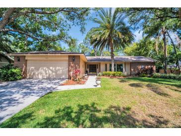 Charming single-story home featuring a brick facade, two-car garage, lush lawn, and mature trees at 495 Palmdale Dr, Oldsmar, FL 34677
