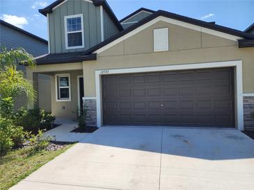 View of the house's garage, siding, stone detail, and driveway with landscaped foliage at 12537 Timber Moss Ln, Riverview, FL 33579