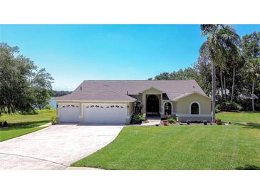 Inviting home featuring a three-car garage, manicured lawn, and beautiful landscaping with a view of the lake at 709 Sportsman Park Dr, Seffner, FL 33584