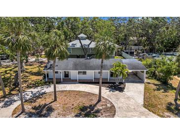 An eye-level view of a white home with a circular driveway and mature palm trees in a lush, tree-filled setting at 8262 26Th N Ave, St Petersburg, FL 33710