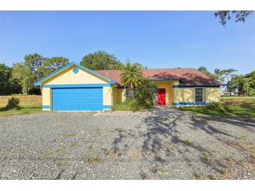 Bright home featuring yellow siding, a blue garage door, red front door and gravel landscaping at 4025 Meadow Run Ln, Wesley Chapel, FL 33543