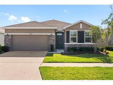 Charming single-story home with a two-car garage, stone accents, and lush landscaping at 13227 Waterleaf Garden Cir, Riverview, FL 33579