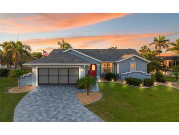 Charming blue single-story home with a red front door, manicured lawn, and a patterned concrete driveway at 220 Singapore Rd, Punta Gorda, FL 33950