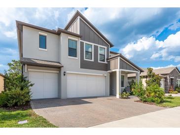 Two-story home featuring a three-car garage, modern facade and a brick-paved driveway and walkway at 21590 Violet Periwinkle Dr, Land O Lakes, FL 34637
