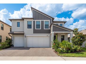 Two-story home featuring a paved driveway leading to a two-car garage, landscaped yard, and modern architectural details at 21590 Violet Periwinkle Dr, Land O Lakes, FL 34637