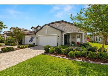 Beautiful single-story home with a stone facade, manicured landscaping, and a brick paved driveway and a three-car garage at 4220 Barletta Ct, Wesley Chapel, FL 33543