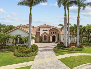 Stunning estate home featuring a terracotta tile roof, lush landscaping, and a brick driveway, surrounded by mature palm trees at 5405 Tybee Island Dr, Apollo Beach, FL 33572