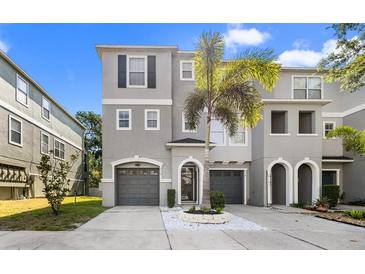 Three-story townhome featuring a gray facade, arched entryway, and a well-maintained driveway with landscaping at 616 Wheaton Trent Pl, Tampa, FL 33619