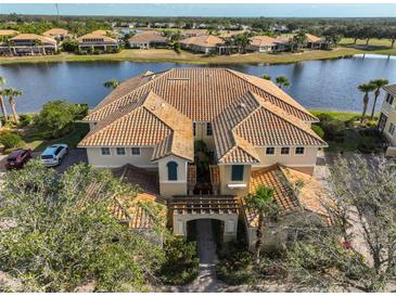 Aerial view of a waterfront condo with a clay tile roof, lush landscaping, and serene lake views at 1348 Emerald Dunes Dr, Sun City Center, FL 33573