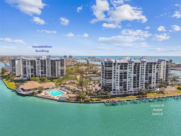 Stunning aerial view of the Constellation building with pool, lush landscaping, and boat docks on shimmering blue water at 9425 Blind Pass Rd # 802, St Pete Beach, FL 33706