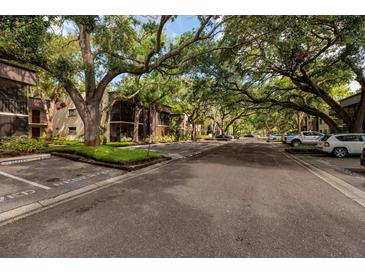 A lush, tree-lined street view showcases the condo buildings and reserved parking spaces at 11708 Raintree Village Blvd # A, Temple Terrace, FL 33617