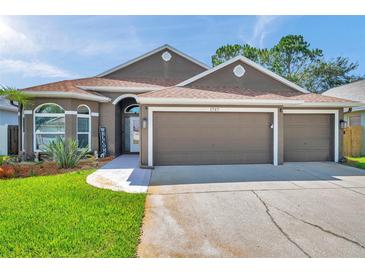 Charming single-story home featuring a well-manicured lawn, three-car garage, and beautiful landscaping at 1747 Wood Brook St, Tarpon Springs, FL 34689
