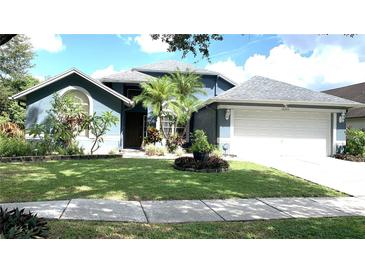 Charming blue home with manicured lawn, mature trees, and attached two-car garage at 16505 Lake Heather Dr, Tampa, FL 33618