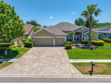 Beautiful home featuring a three-car garage, paver driveway, manicured lawn, and mature landscaping at 6104 Cognac Cir, Lutz, FL 33558