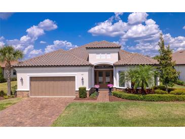 Inviting single-story home featuring a barrel tile roof, brick driveway, and meticulously manicured landscaping at 11411 Juglans Dr, Odessa, FL 33556