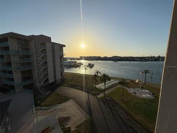 Scenic waterfront view overlooking the channel, featuring a condo building and palm trees silhouetted against the sunset at 1 Key Capri # 502E, Treasure Island, FL 33706