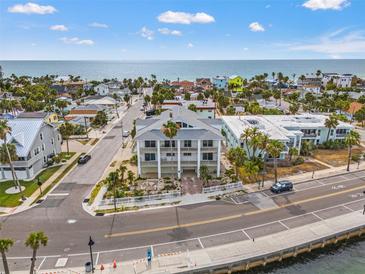 An exterior showcases a three-story beach house, white columns, and balconies, offering stunning coastal living at 1104 Pass A Grille Way, St Pete Beach, FL 33706