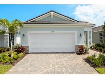 Charming home featuring a two-car garage, lush landscaping, and a brick-paved driveway at 11359 Boundless Ter, Venice, FL 34293