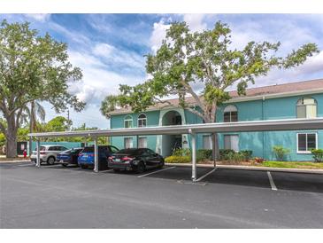 Exterior of condo building with covered parking, teal paint, landscaping, and white trim against a partially cloudy blue sky at 11404 2Nd N St # 3, St Petersburg, FL 33701