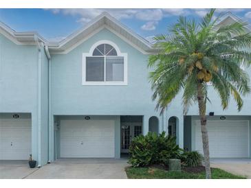 Inviting light blue two-story townhome with white garage doors, palm tree, and lush landscaping at 623 Garland Cir, Indian Rocks Beach, FL 33785