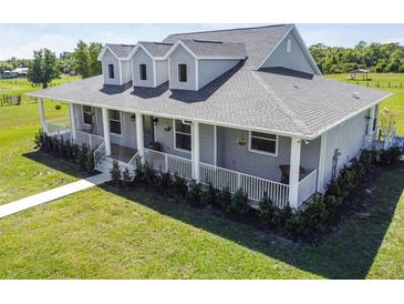 Inviting gray home with a charming wraparound porch, white railings and dormer windows at 7627 Artifact Dr, Zephyrhills, FL 33541