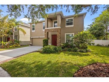 Two-story tan house with a stone pillar front porch, attached garage, and landscaped yard at 19101 Marisa Ridge Pl, Tampa, FL 33647