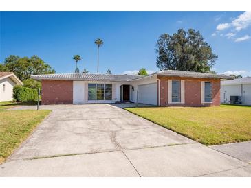 Charming single-story home featuring a brick facade, concrete driveway, and well-maintained lawn under a clear blue sky at 14921 Crown Dr, Largo, FL 33774