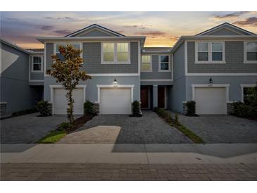 Charming townhome with gray siding, a one-car garage, and a well-maintained paver driveway under a sunset sky at 2529 Arbor Wind Dr, Lutz, FL 33558