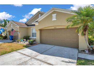 Tan home featuring a brown garage door, palm tree, well manicured lawn and a sunny sky at 30327 Lettingwell Cir, Wesley Chapel, FL 33543