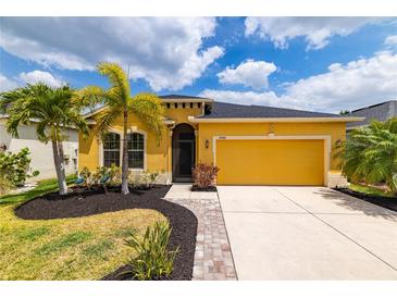 Inviting yellow home featuring a 2-car garage, well-manicured lawn and lush, mature palm trees at 5048 Inshore Landing Dr, Apollo Beach, FL 33572