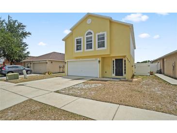 Bright yellow two-story home with a two car garage, black door, and well-maintained lawn at 11323 Ivy Flower Loop, Riverview, FL 33578