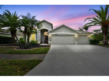 Beautiful home featuring a three-car garage, stone accents, and lush tropical landscaping at 8208 Pinewood Run Ct, Tampa, FL 33647