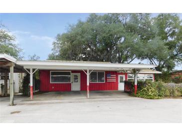 Charming single-story red house with a covered parking area and an American flag at 3940 E Knights Griffin Rd, Plant City, FL 33565