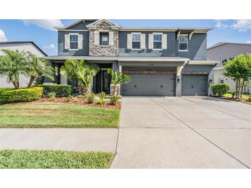 Two-story home featuring a three-car garage, stone accents, well-manicured landscaping, and decorative shutters at 4094 Windcrest Dr, Wesley Chapel, FL 33544