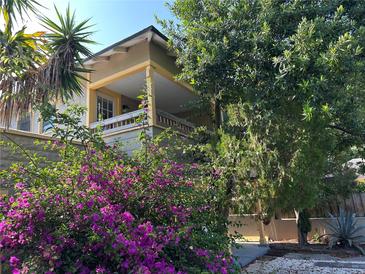 Charming two-story home featuring a covered porch, lush landscaping, and vibrant purple flowers at 943 7Th N St, St Petersburg, FL 33701