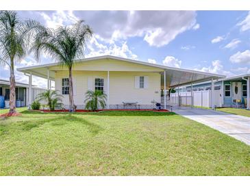 Charming manufactured home featuring a well-maintained lawn, carport, and lush palm trees at 5721 Apache St, Zephyrhills, FL 33542