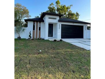Modern home featuring black garage door, stylish white facade, and freshly cut lawn at 907 E Okaloosa Ave, Tampa, FL 33604
