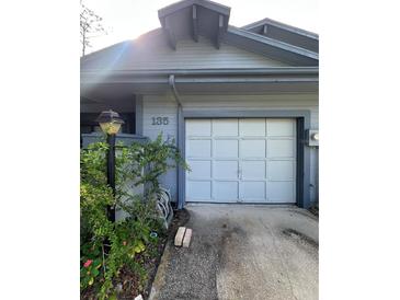 Shows a one-car garage on a blue house with green plants in front at 135 Pinewinds Blvd, Oldsmar, FL 34677