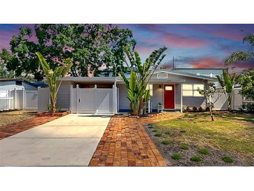 Charming one-story home with a red door, well-manicured lawn, tropical landscaping, and driveway at 4735 W Oklahoma Ave, Tampa, FL 33616