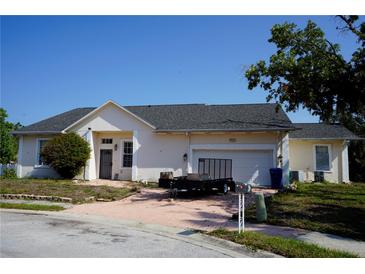 Beige single-story home with a two-car garage, brick driveway, and well-maintained landscaping at 12349 Wasatch Ct, New Port Richey, FL 34654