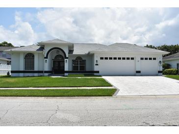 Inviting white home featuring a well-manicured lawn and a three-car garage at 1961 Dunbrody Ct, Dunedin, FL 34698