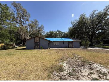 View of the home featuring a stucco exterior, blue tarp on the roof, and mature trees in a spacious yard at 37810 Silver Pines Ave, Zephyrhills, FL 33542