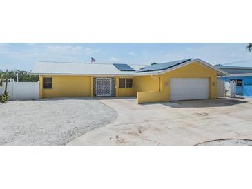 Charming yellow home featuring a metal roof, solar panels, white rock landscaping, and a paved driveway at 1421 Sea Gull S Dr, St Petersburg, FL 33707